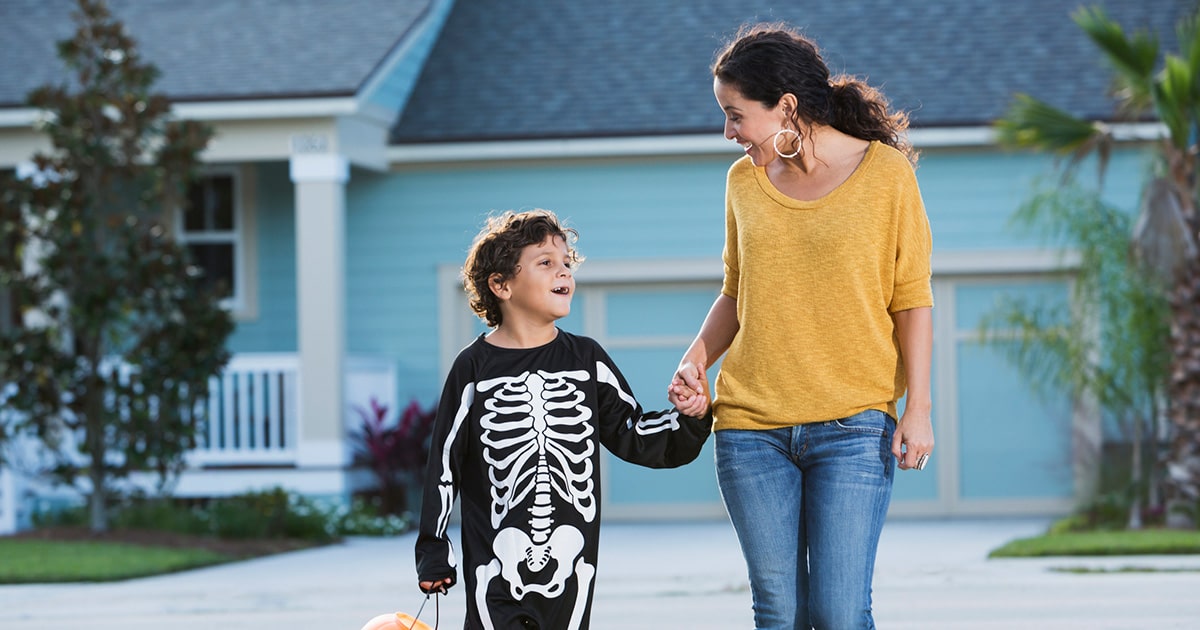 A mother holds hands with her son, who’s wearing a skeleton Halloween costume